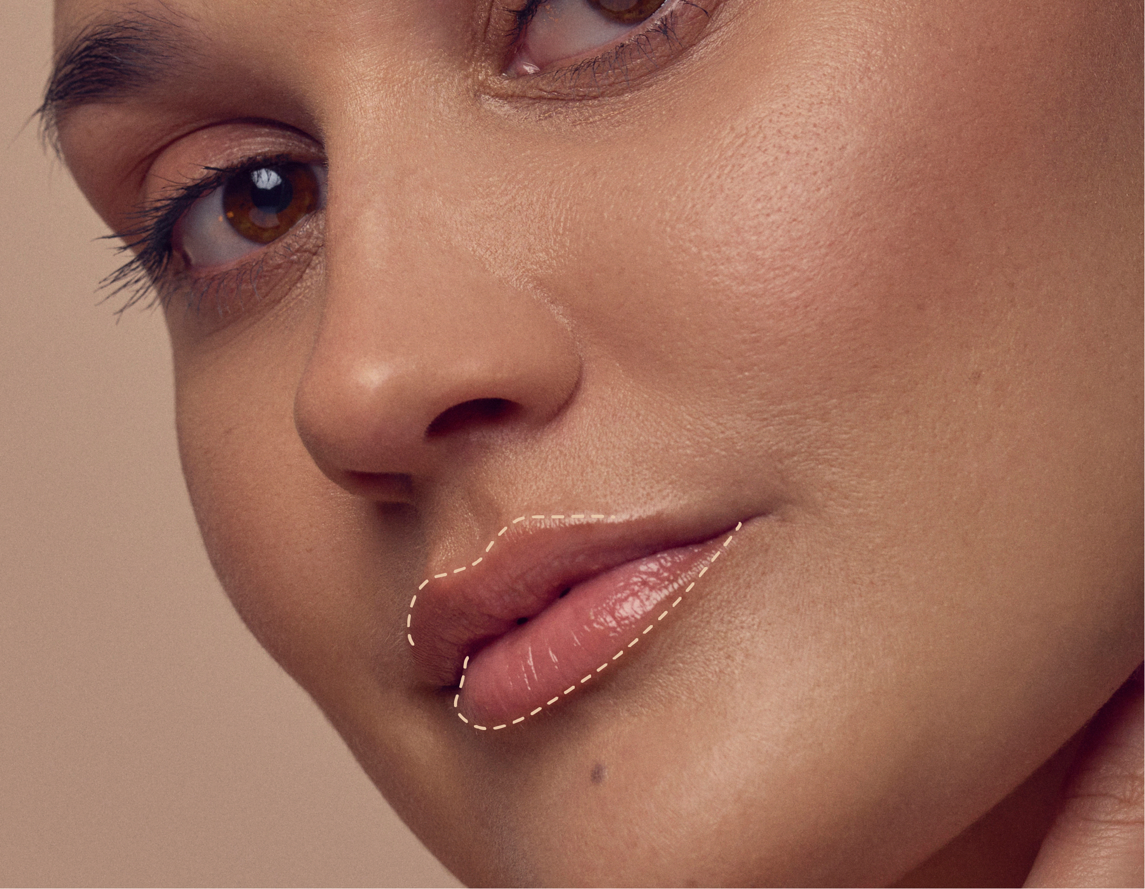 Close-up of a persons face showing smooth, glowing skin and subtle makeup. A dashed line highlights the lips, which have a glossy finish, against a neutral background.
