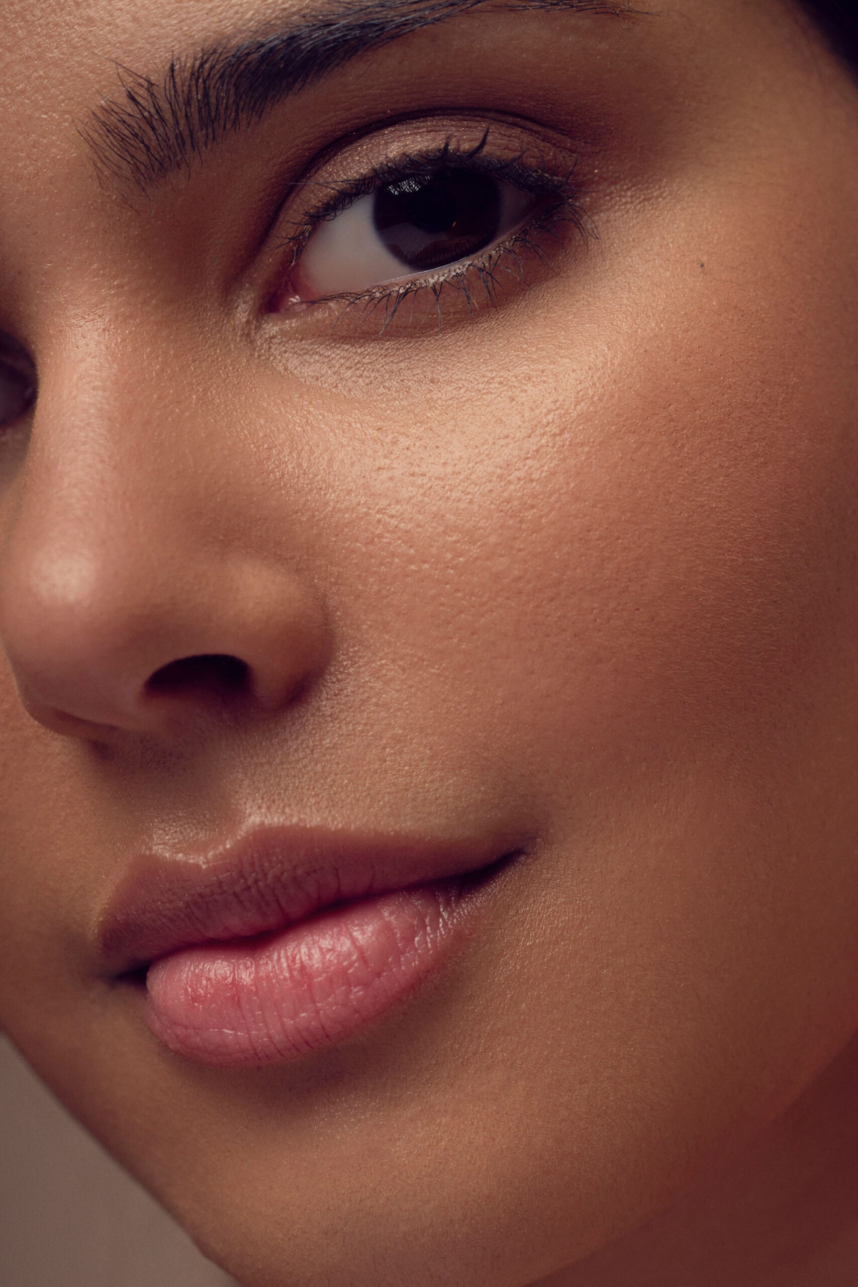 Close-up of a persons face focusing on the eye and lips. The skin appears smooth, with natural makeup. The image emphasizes the details of the eyelashes, eyebrows, and the curve of the lips.