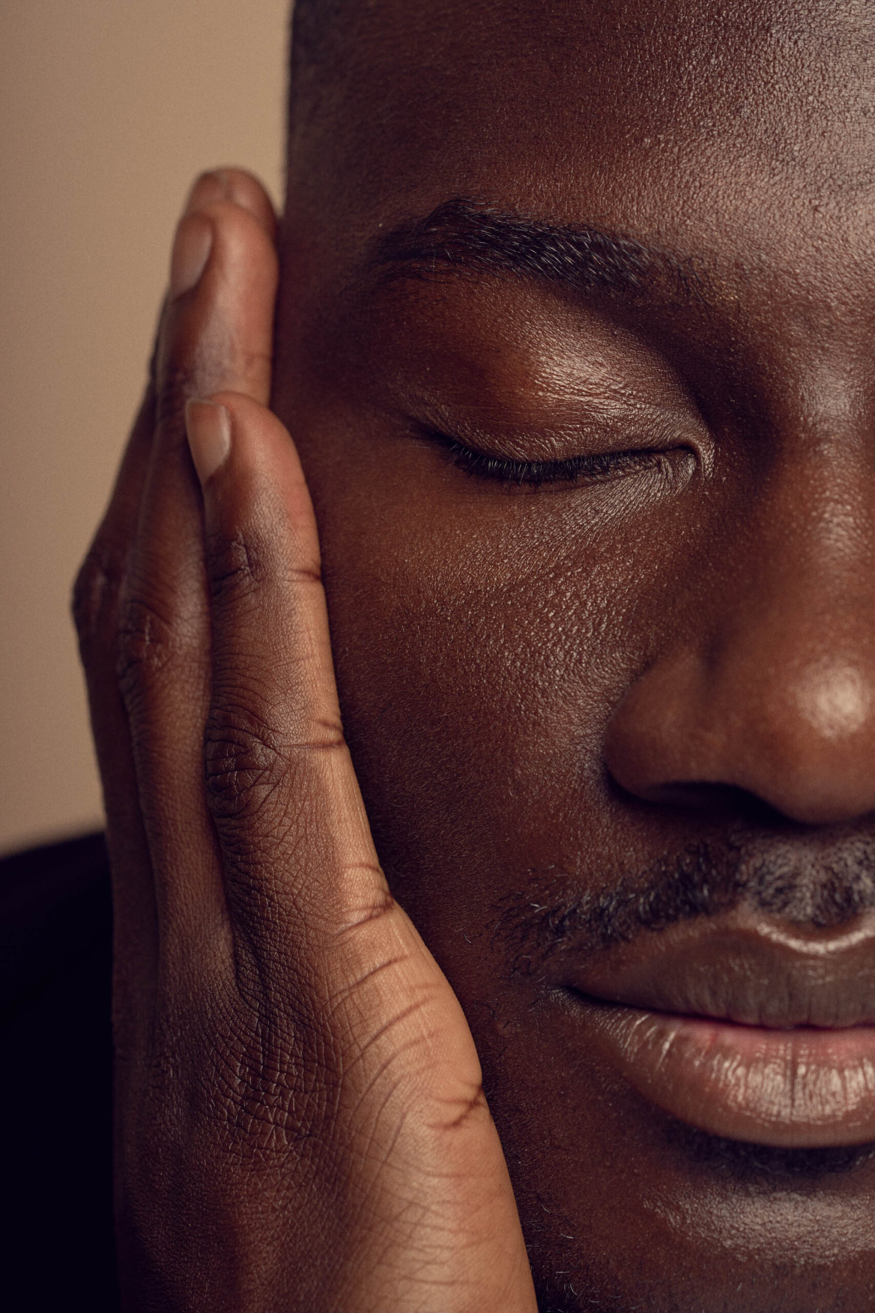 A close-up of a person with closed eyes, resting their cheek on their hand. The lighting is soft, highlighting their serene expression and smooth skin texture. The background is out of focus, drawing attention to the face.