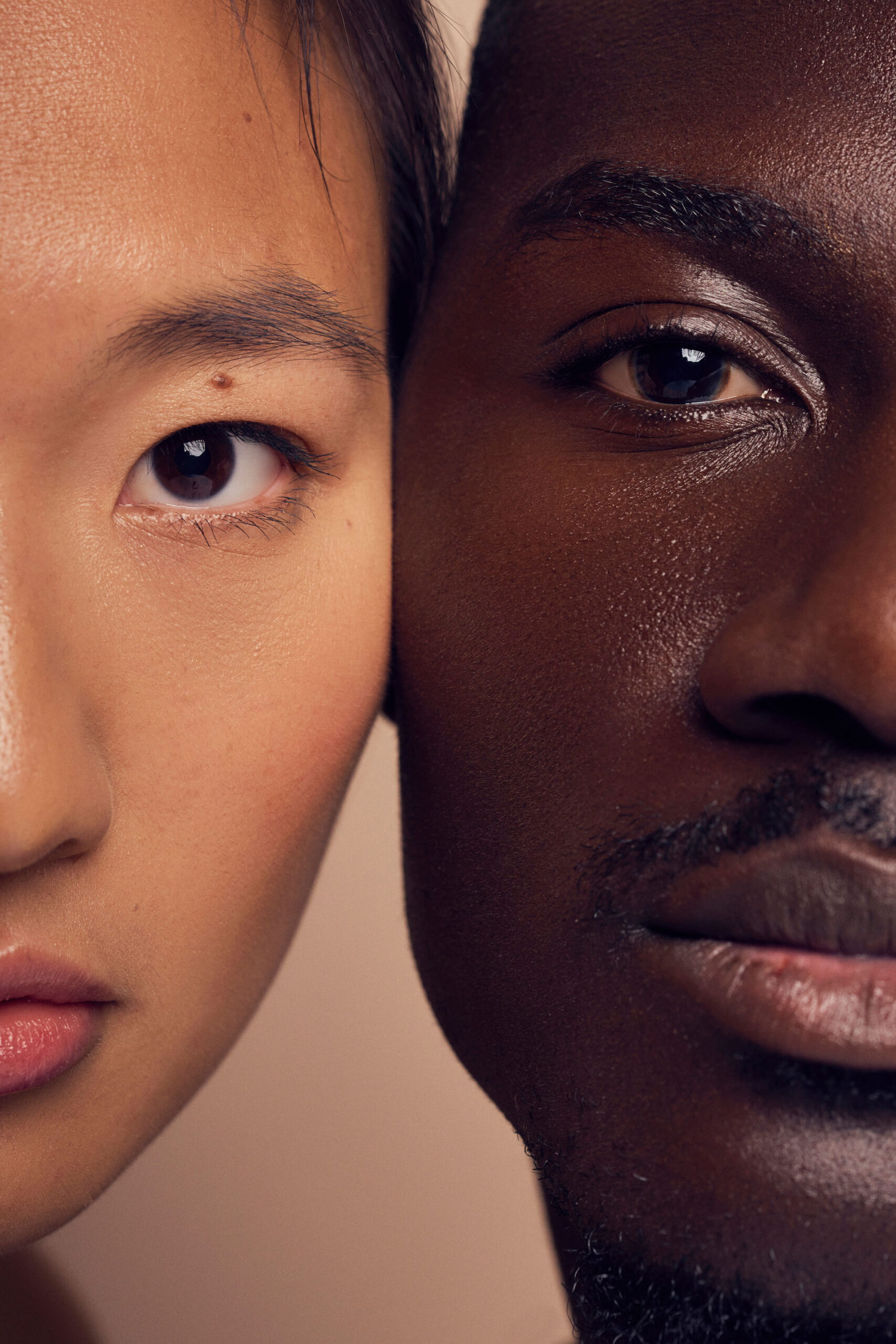 A close-up of two people, one with light skin and one with dark skin, showing their faces side by side. The image focuses on their eyes, nose, and lips, highlighting diversity and contrast in skin tones.