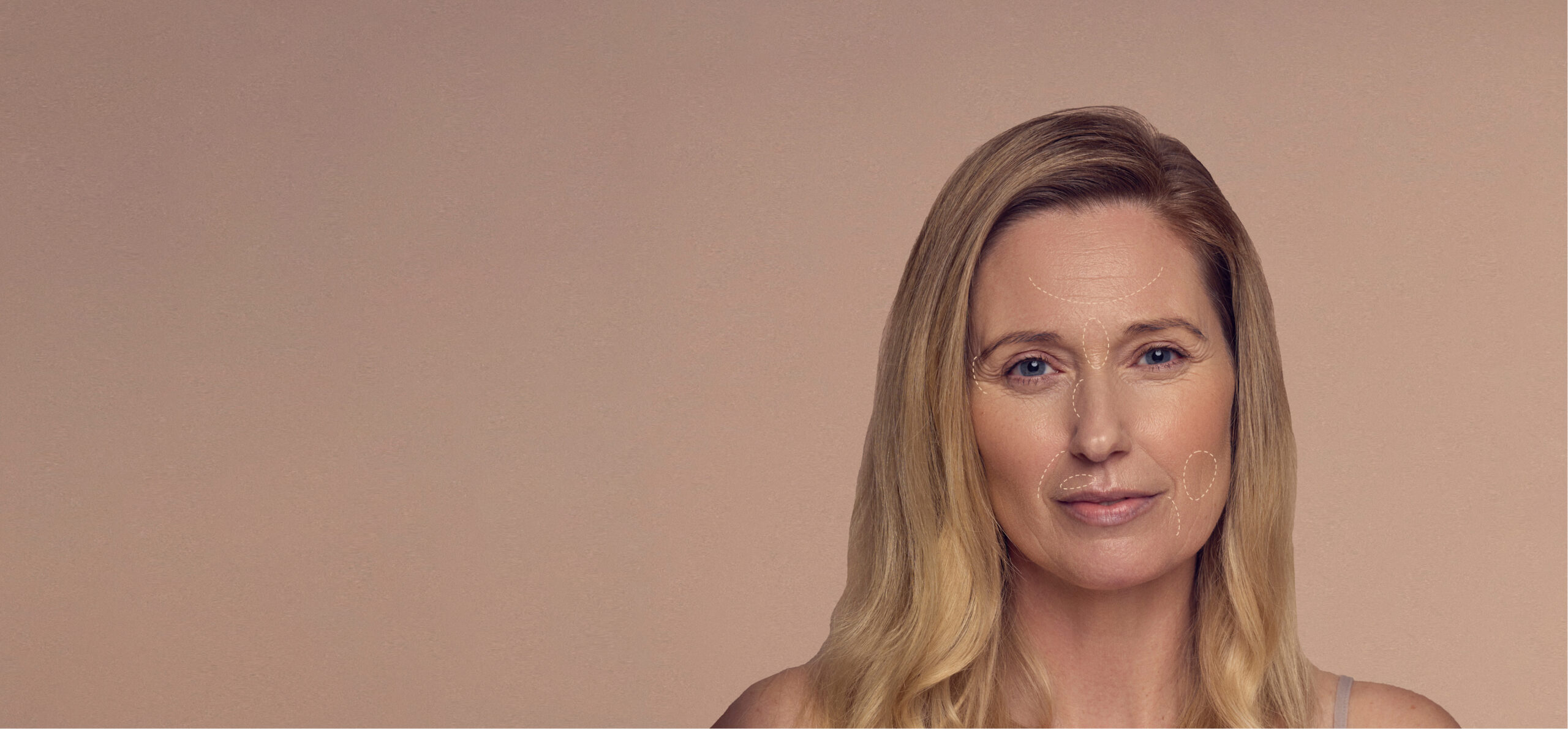 A woman with long blonde hair stands against a light brown background. Her face features subtle contour lines marked with makeup. She wears a neutral expression.