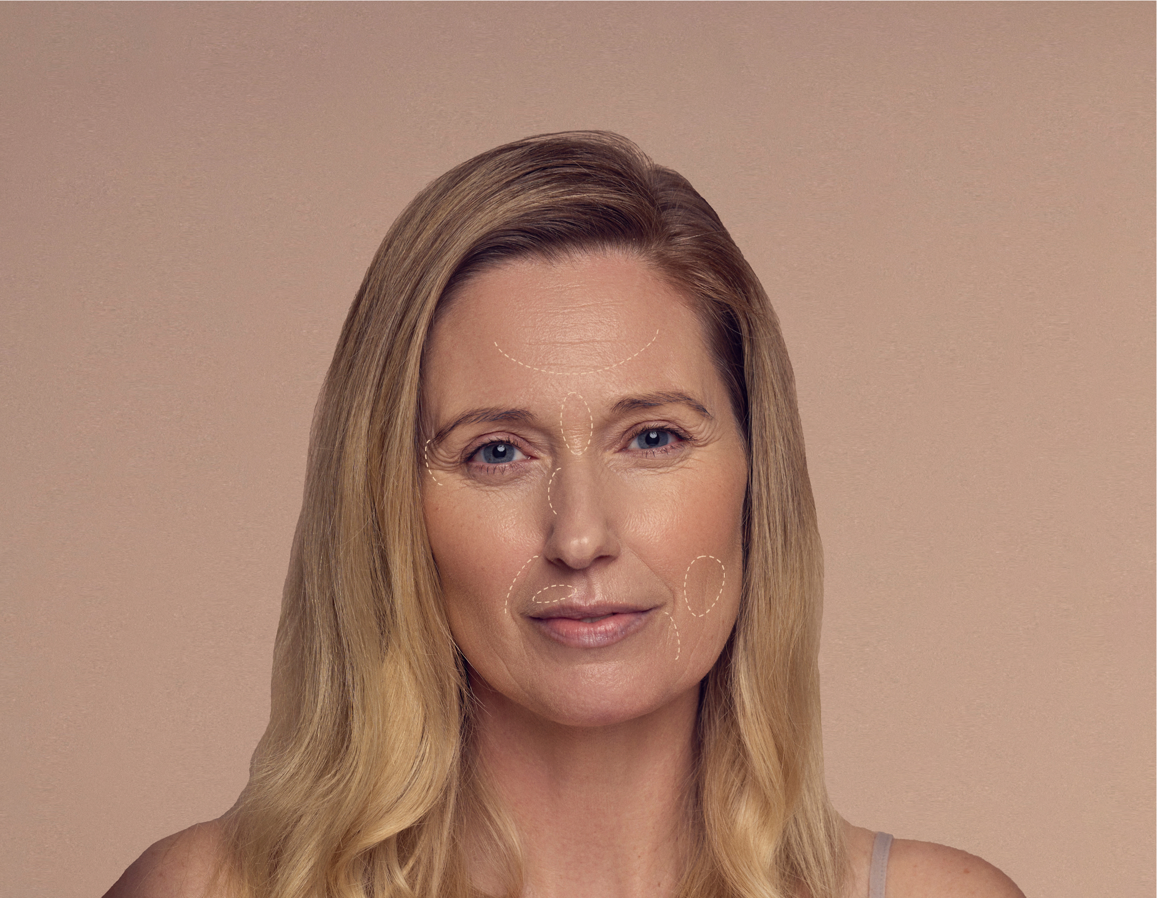 A woman with long blonde hair looks directly at the camera. She has contour lines drawn on her face aiming to highlight her features. The background is a neutral beige color. She appears calm and confident.